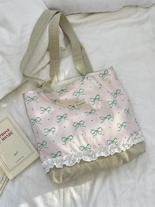 Pink canvas tote bag with green bow print and white lace trim shown on soft bedding