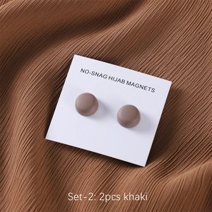 Close-up of two khaki matte magnetic hijab clips on card over brown fabric background