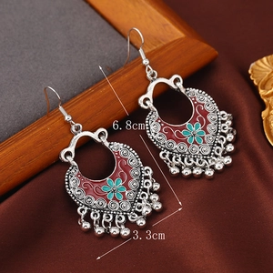 Detail view of silver vintage earrings with red enamel flowers and bell tassel on wood