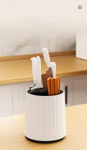 Close-up of a white rotating kitchen knife block with vertical stripes on a wooden counter