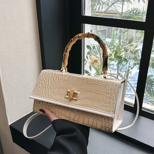 Detail of beige faux leather handbag with crocodile pattern and bamboo top handle