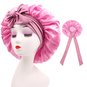 Close-up of pink satin sleep cap with adjustable long ribbons and bow detail