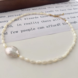Macro detail of white freshwater pearl necklace with large baroque pearl and gold clasp