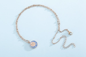 Macro detail of rose gold Gemini coin pendant with blue enamel on a beaded double chain