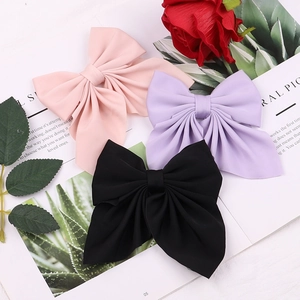Detail of pink, purple, and black bow hair clips in matte fabric on a floral background