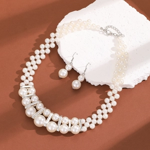 Macro detail of multi-layer pearl necklace and earrings set on textured stone base
