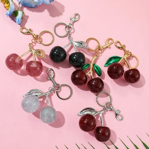 Detailed flat lay of luxury cherry keychains in red, black and silver on pink background