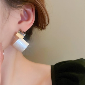 Detailed view of large geometric diamond earrings with brushed texture on model