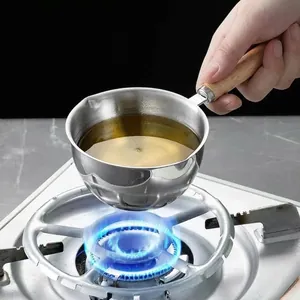 Polished stainless steel small oil pan with wooden handle heating over a gas stove flame