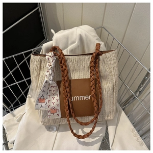 Détail d'un cabas en paille tissée avec empiècement en cuir brun et foulard décoratif
