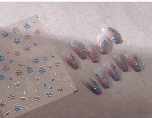Dettaglio degli adesivi per unghie con fiori blu e viola e bordi argentati su base beige