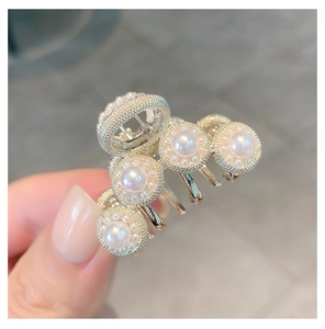Detail view of a gold hair claw clip featuring elegant white pearl flower motifs