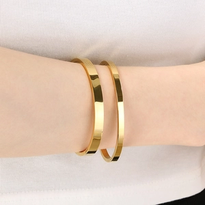 Minimalist glossy gold stainless steel bangles set worn on wrist over white knitwear