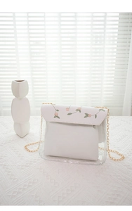 Detail of floral embroidery on transparent crossbody bag with white flap and gold chain