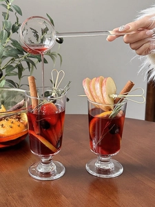 Action shot of glass spoon pouring warm mulled wine into a clear stemmed cocktail glass