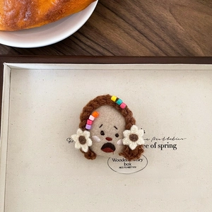 Detailed close-up of handmade crochet brooch featuring a whimsical doll with floral accents