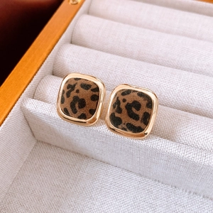 Close-up of leopard print square stud earrings with gold trim on beige display