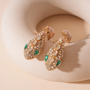 Close-up of golden snake-style drop earrings with green crystals and pearls