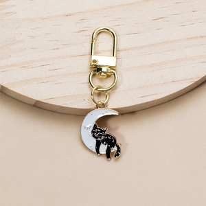 Close-up of black cat on white moon enamel keychain with golden clip on wood surface