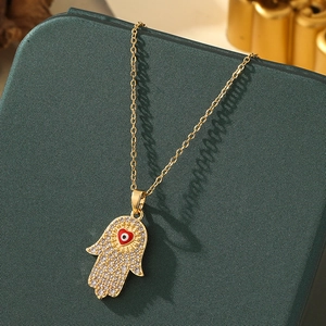 Detailed close-up of golden Hamsa Hand necklace with red heart and evil eye detail