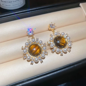 Macro view of vintage sunflower stud earrings with amber tiger eye and pearls on a cushion