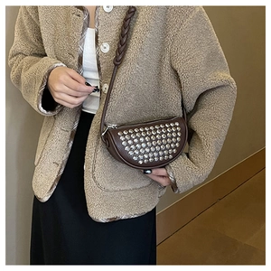 Detailed close-up of brown leather crescent bag with silver rivets and woven strap on model
