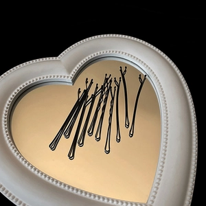 Close-up of matte black metal bobby pins with wavy texture on a heart-shaped mirror