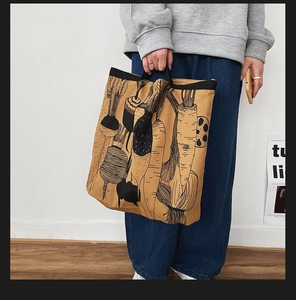 Close-up of khaki canvas tote bag with vegetable print held by model in casual outfit