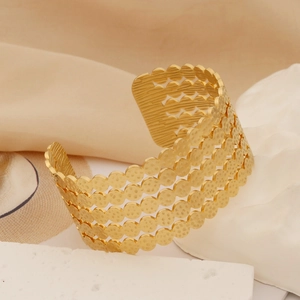 Macro detail of gold open wide bangle featuring wavy dot cutout pattern on a textured stone