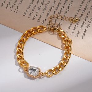Detail eines goldenen Panzerarmbands mit quadratischem Edelstein auf Buchseiten