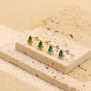 Macro view of emerald drop earrings with gold and silver bases on beige stone