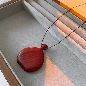 Close-up of vintage wooden flask pendant with brown hand-woven cord on velvet tray