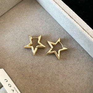 Detail of star-shaped gold earrings with polished finish on a soft grey velvet background