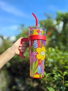 Outdoor shot of a 40oz stainless steel floral tumbler with handle and red straw