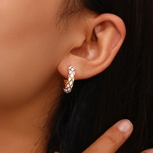Detailed view of white enamel C-hoop earrings with golden grid pattern on model