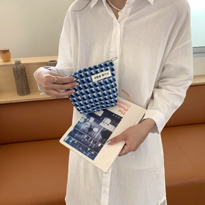Détail de la trousse tissée à carreaux bleus tenue en main avec fermeture éclair métallique