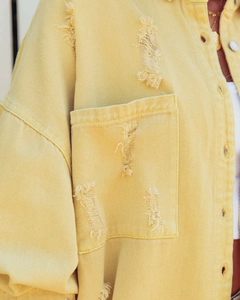 Detail shot of frayed holes and denim texture on yellow long sleeve denim jacket