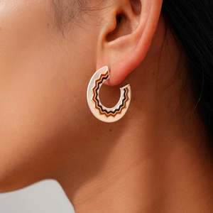 Detail of C-shaped hoop earrings with brown wave patterns worn by a model