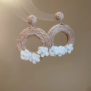 Detail of bohemian rattan circle earrings with white fabric floral accents on stand