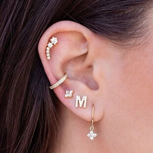 Detailed close-up of golden M-shaped earring with zircon micro-paving on a model