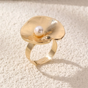 Close-up of golden wavy metal ring with a white pearl inlay on a stone background