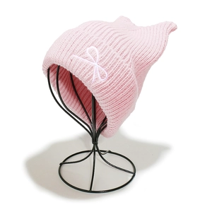 Detail of pink knitted beanie with cat ear design and white bow embroidery on mannequin