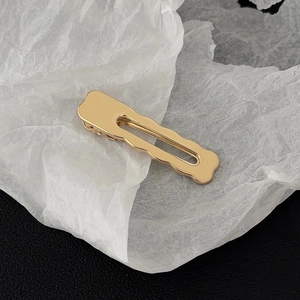 Macro detail of golden metal hair clip with wavy edges and hollow design on paper