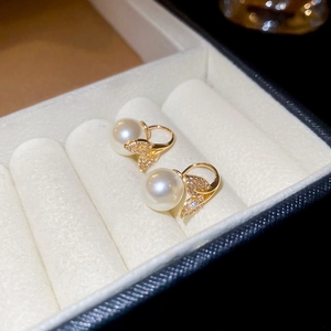 Macro shot of elegant gold pearl earrings with zircon leaf details on white velvet