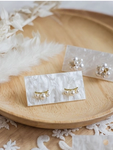 Elegant pearl stud earrings set on marble card and wooden tray with dry flowers