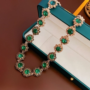 Close-up of vintage gold flower necklace with green gemstones on a jewelry box