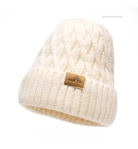 Macro detail of beige chunky knit beanie with textured cable pattern and leather patch