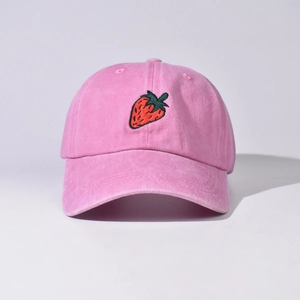 Dettaglio di un cappello da baseball in cotone lavato rosa con ricamo a fragola.