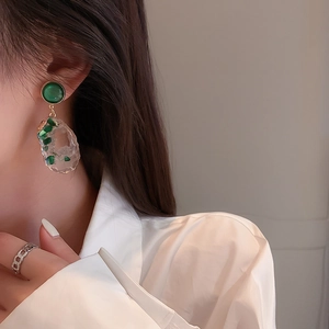 Detail of irregular hollow earrings with emerald green stone accents and gold plating