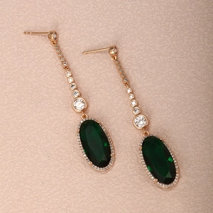Macro detail of gold-plated long drop earrings with emerald stones and white zircons